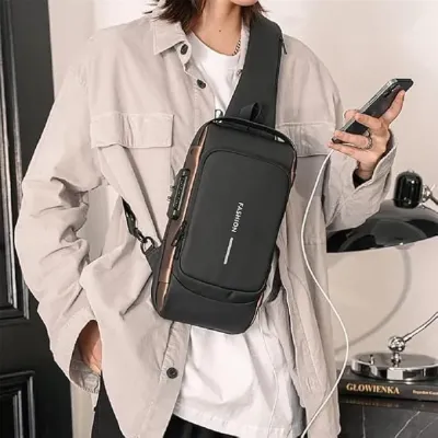 Person wearing the Anti Theft Sling Bag across chest, charging a mobile phone via integrated USB port