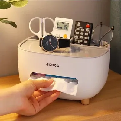 Hand pulling a paper tissue from a white Ecoco Tissue Box with small wooden legs on a wooden table.