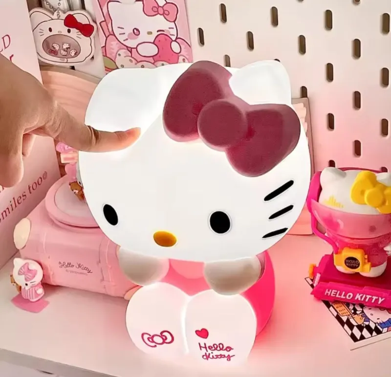 Hand tapping the glowing white Hello Kitty Silicone Night Lamp on a pink desk setup.