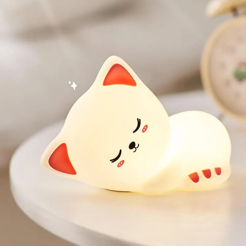 Warm glowing silicone cat night lamp in a cute sleeping pose resting on a white bedside table.