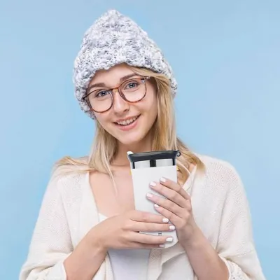 Smiling woman holding the Vacuum Insulated Coffee Mug 350ml wearing a beanie and glasses